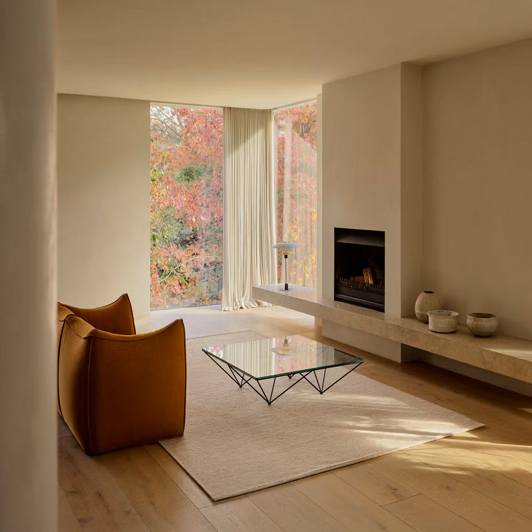 Modern living room with a fireplace, glass coffee table, and autumn foliage outside. Aspen_Sandstorm rug