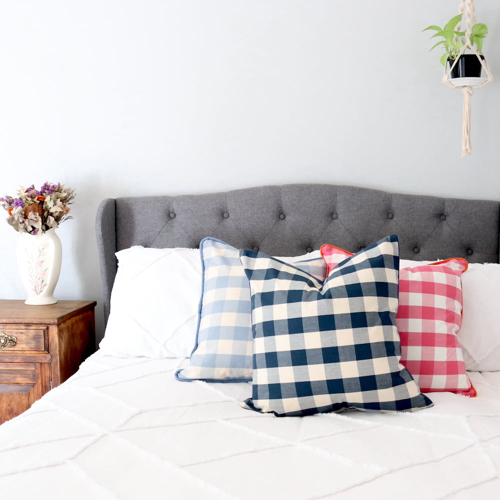 Perwinkle, Navy & Pink Gingham cushions on a bed with an upholstered bedhead. 
