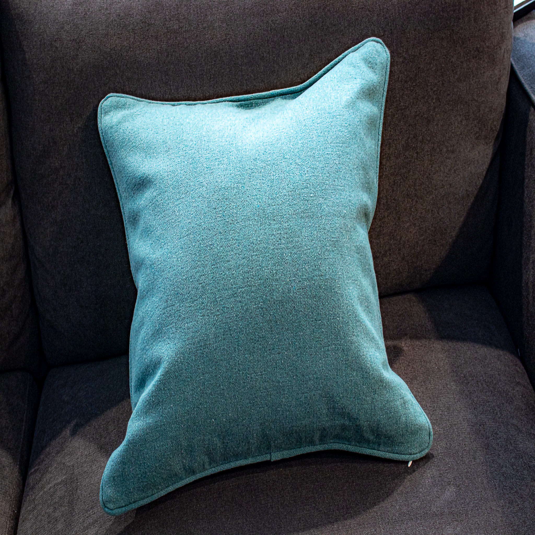 Luxe and Humble reversible cushion showing its solid teal fabric side with soft texture and neat piping, placed on a dark sofa for a versatile, modern home styling accent.