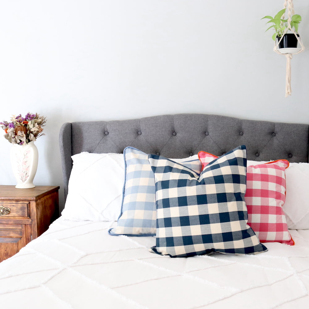 Periwinkle, Navy & Pink Gingham cushions on a Grey Upholstered bed with white boho fringed cover.