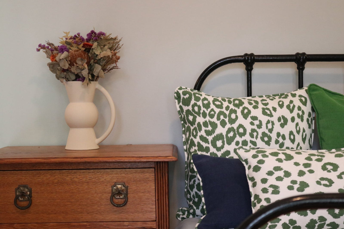 In situ image of the 50cm x 50cm Bespoke Scatter Cushion Featuring Schumacher's Iconic Leopard in Green on a wrought iron bed.