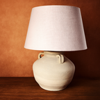 Wabi - Sabi Table lamp with a white ceramic base and beige lampshade on a wooden surface against an orange wall.