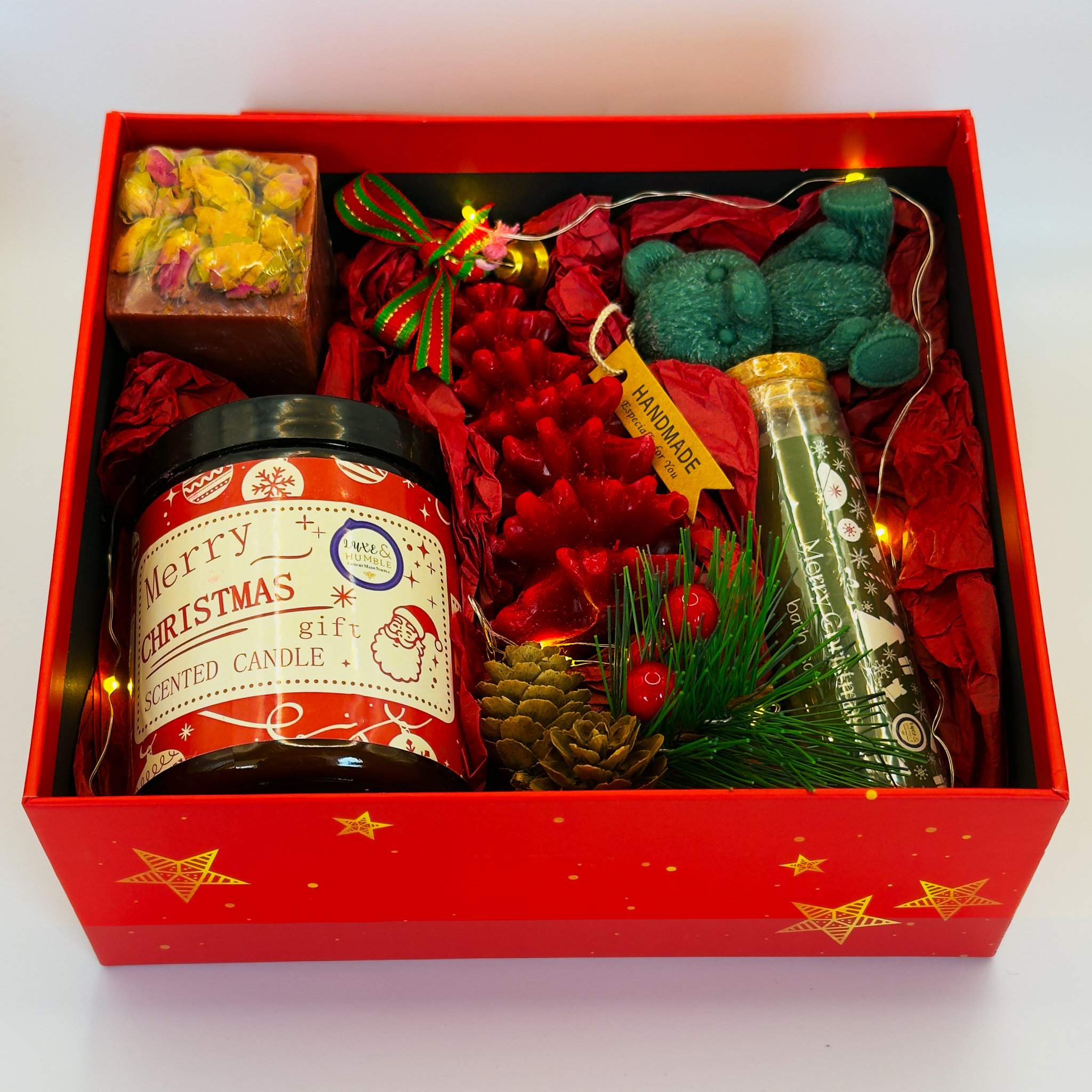 A red Luxe & Humble Christmas hamper containing a Merry Christmas scented candle, handmade floral soap, red tree candle, teal teddy bear and a holiday bath soak. Styled on a clean white background, ideal for Australian Christmas gifting, pamper boxes and festive wellness sets.