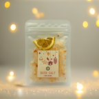 A Luxe & Humble Citrus Glow Christmas Bath Salt presented in a clear stand-up pouch filled with natural mineral salts and dried citrus slices. The festive label features hanging Christmas ornaments, stars and a gift illustration. Styled with warm golden bokeh lights and soft sparkles, this image evokes a cosy, luxurious Christmas feel—perfect for Australian gifting, stocking fillers and self-care lovers.