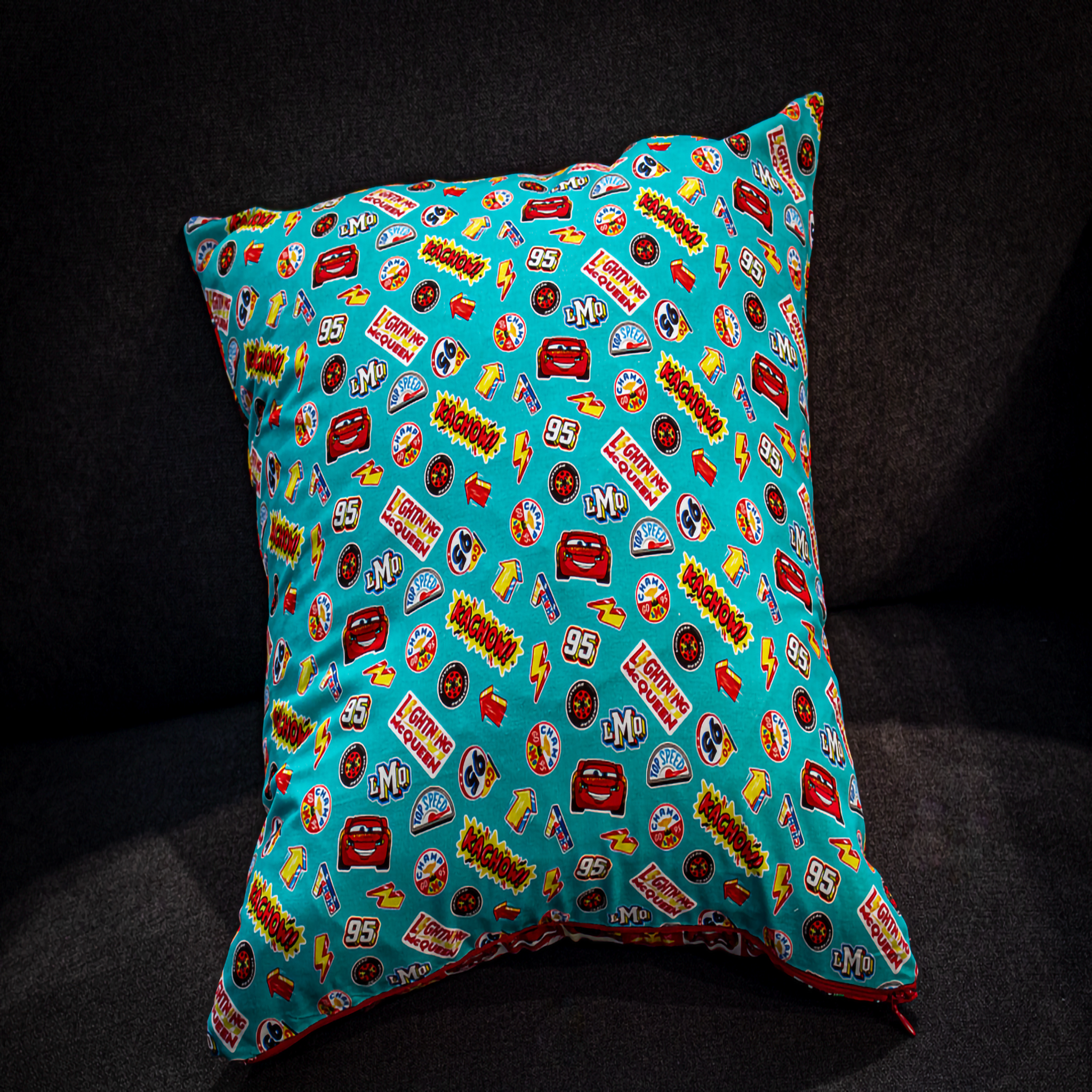 Disney cars cushion with teal side featuring Lightning McQueen and reversible red and white checkered pattern.