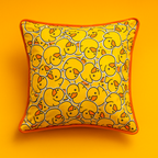 A close-up of the Duckie Print Cushion, showing the cheerful yellow duckling pattern and contrasting orange piping, displayed on a dark sofa.