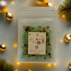 A Luxe & Humble Festive Forest  Christmas Bath Salt displayed in a clear pouch filled with green crystal salts and warm mineral tones. Styled with gold Christmas baubles, pine branches and glowing festive lights. A handcrafted Australian bath salt perfect for Christmas gifting and holiday self-care.