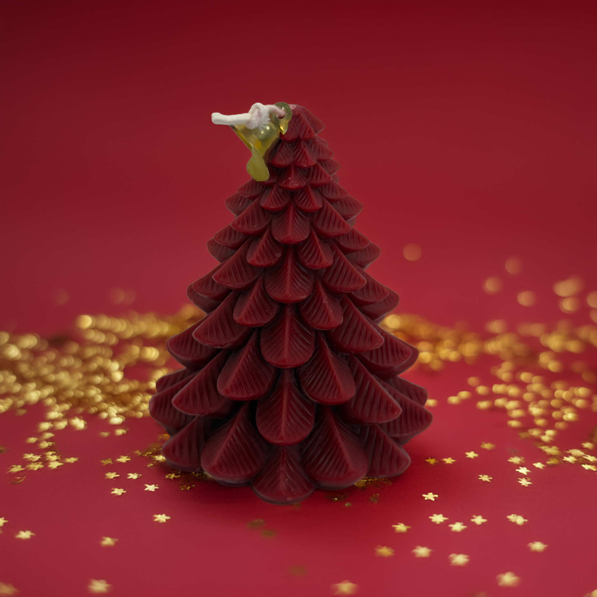 A deep red Christmas tree-shaped candle displayed on a luxe red background with gold star confetti. Perfect for Australian Christmas décor, gifting, and holiday styling. High-quality festive candle from Luxe & Humble Australia.