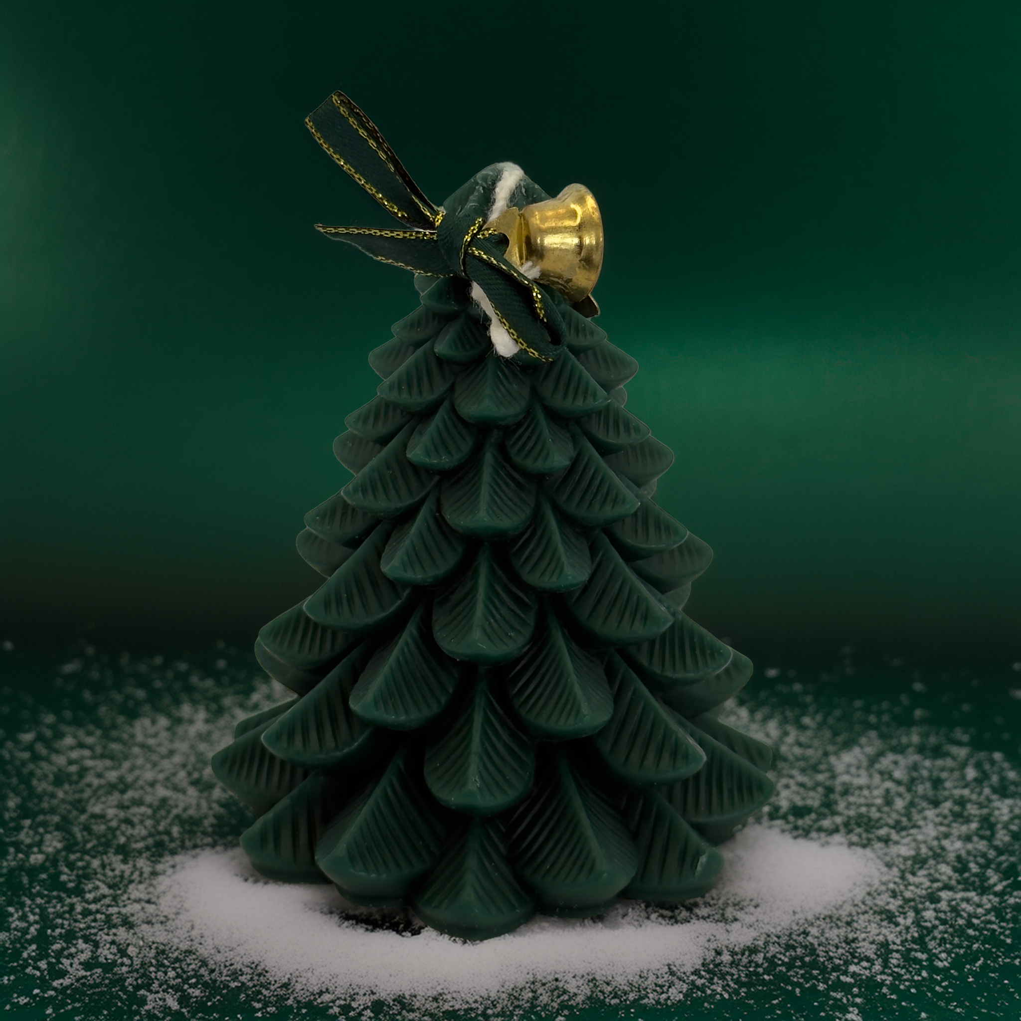 A deep green Christmas tree candle with a gold bell and green ribbon, styled on a snow-dusted surface with a rich green backdrop. A luxe, festive décor candle perfect for Australian Christmas gifting and home styling. Available from Luxe & Humble.