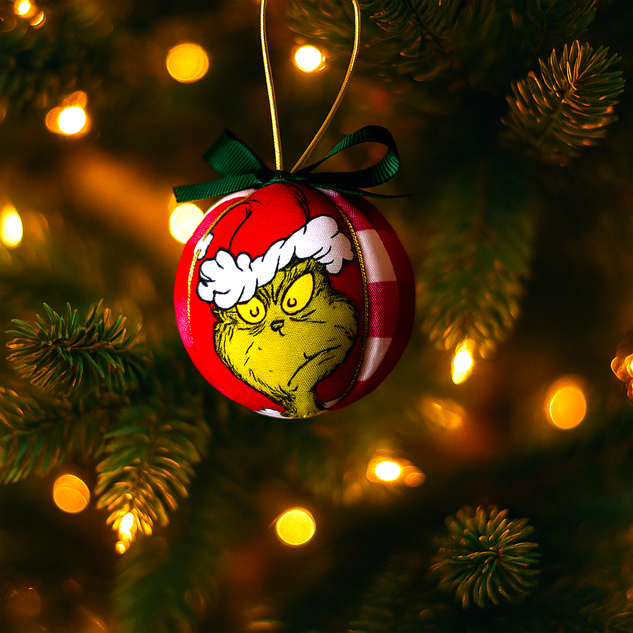 A handmade Grinch bauble ornament featuring the iconic green Grinch face with a Santa hat, hanging from a Christmas tree branch with glowing fairy lights. This festive ornament from Luxe & Humble’s Christmas Collection adds playful charm and personality to any holiday décor.