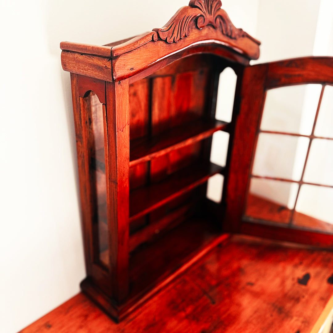 Ornate wooden wall cabinet with glass-pane door and carved arch, sitting on warm timber table