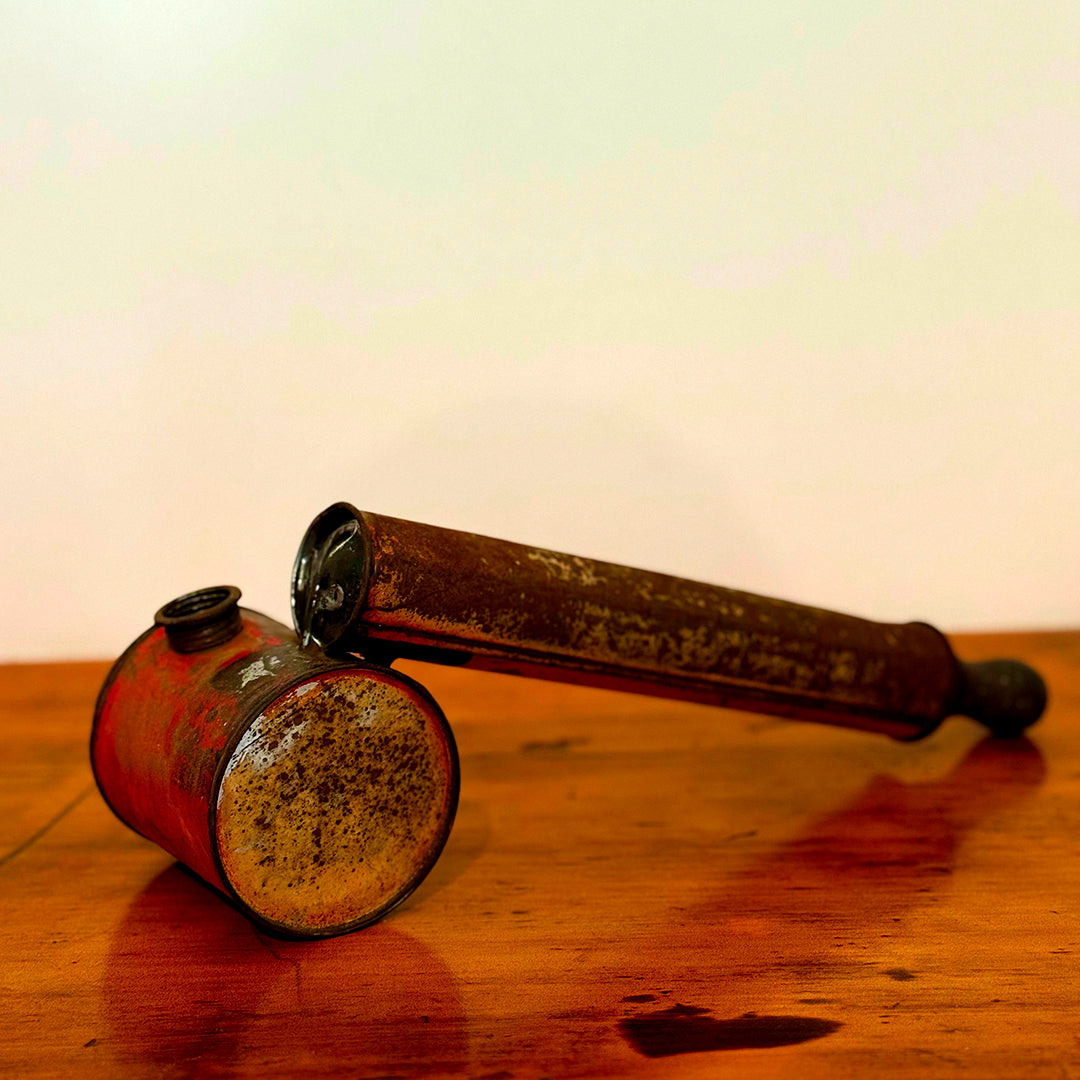 Vintage insect spray hand pump with a rusty red finish, displayed on a wooden surface, showcasing its aged, distressed appearance.