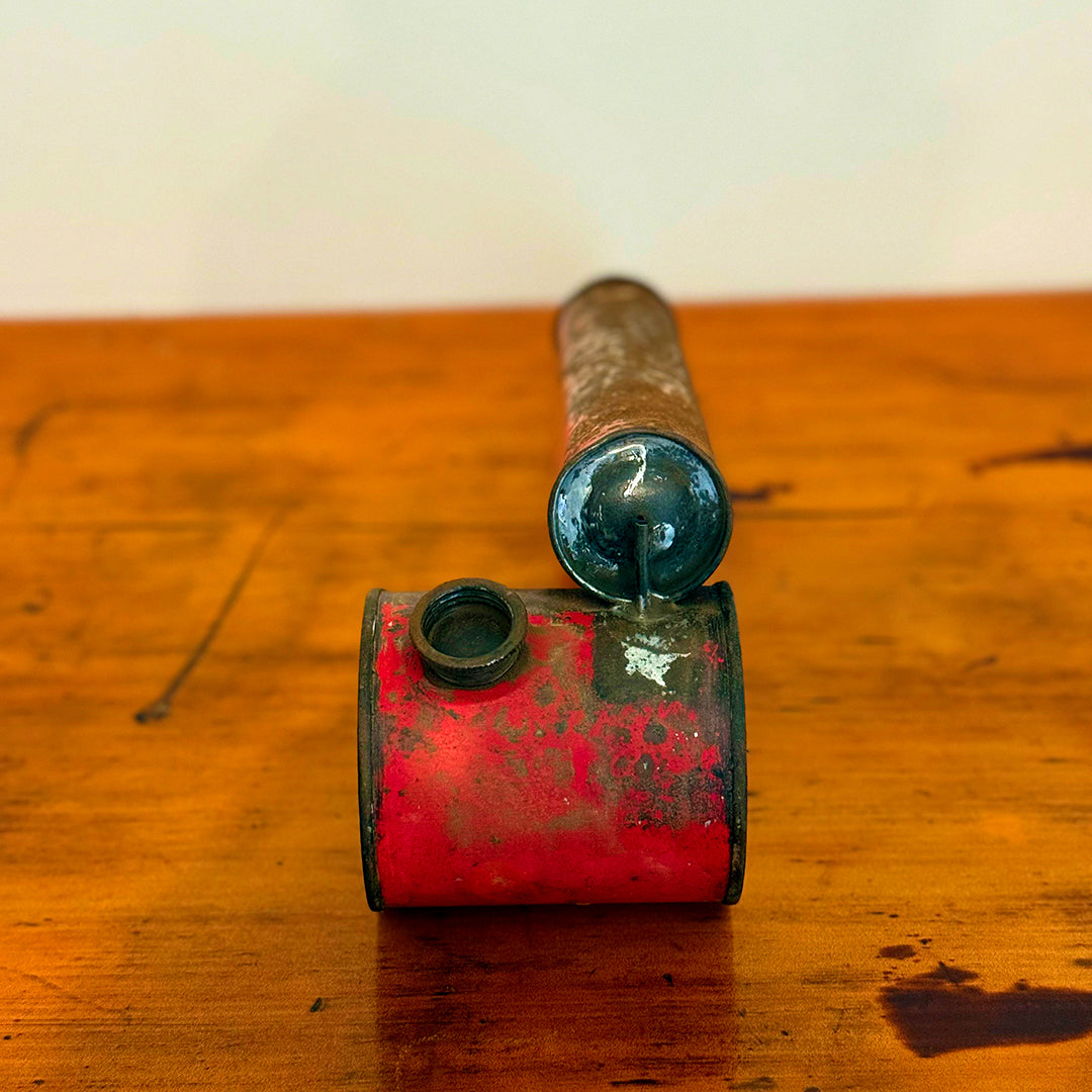 Vintage insect spray hand pump with a rusty red finish, displayed on a wooden surface, showcasing its aged, distressed appearance.