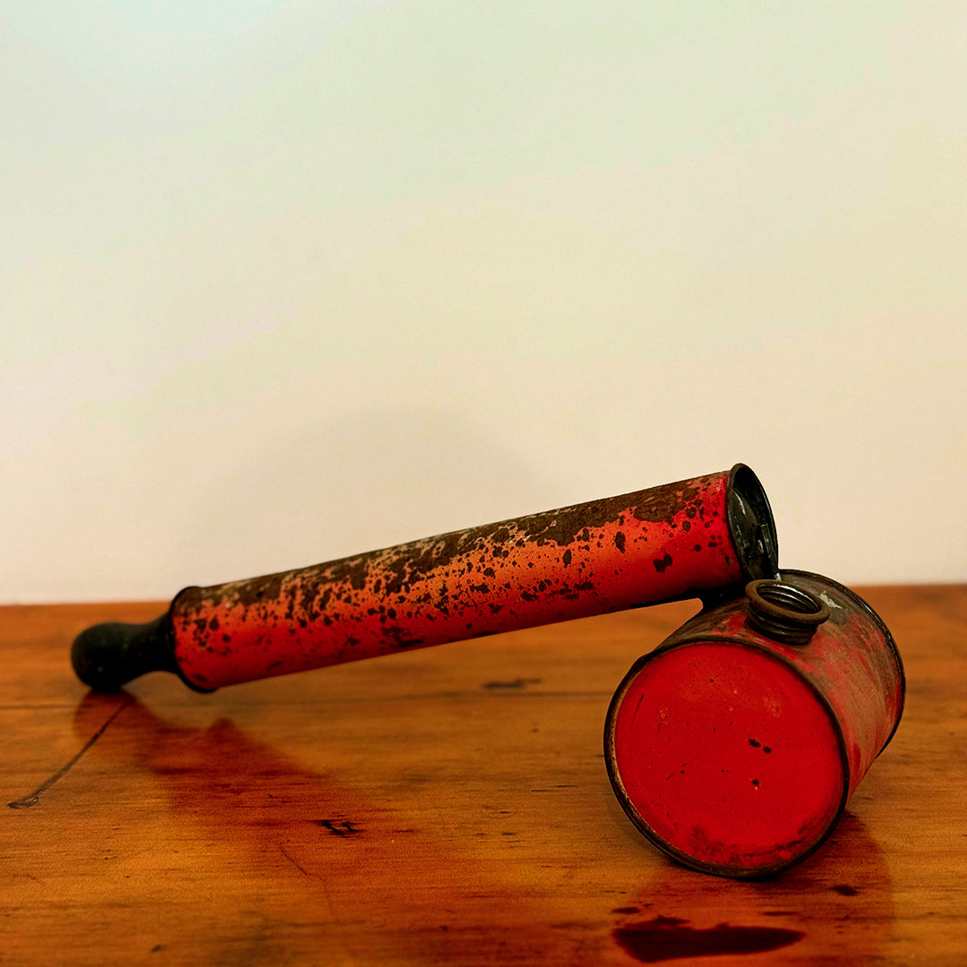 Vintage insect spray hand pump with a rusty red finish, displayed on a wooden surface, showcasing its aged, distressed appearance.