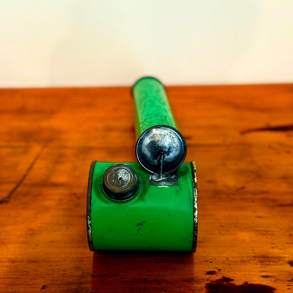 Vintage green insect spray hand pump with a shiny metal cap, displayed on a wooden surface, showcasing its smooth green finish and retro design.