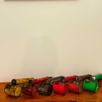 Collection of vintage hand pump insect spray metal cans with different colors on a wooden surface against a white wall.