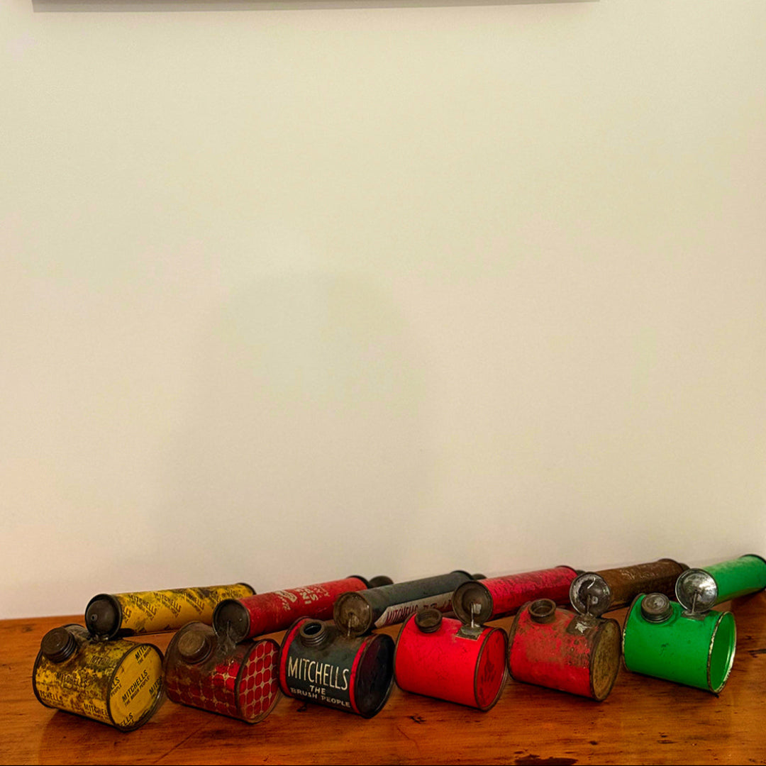 Collection of vintage hand pump insect spray metal cans with different colors on a wooden surface against a white wall.
