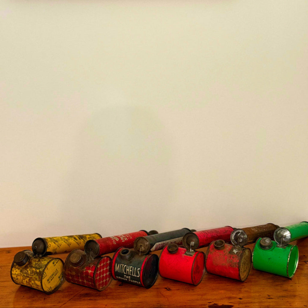 Collection of vintage metal cans with different colors on a wooden surface against a white wall.