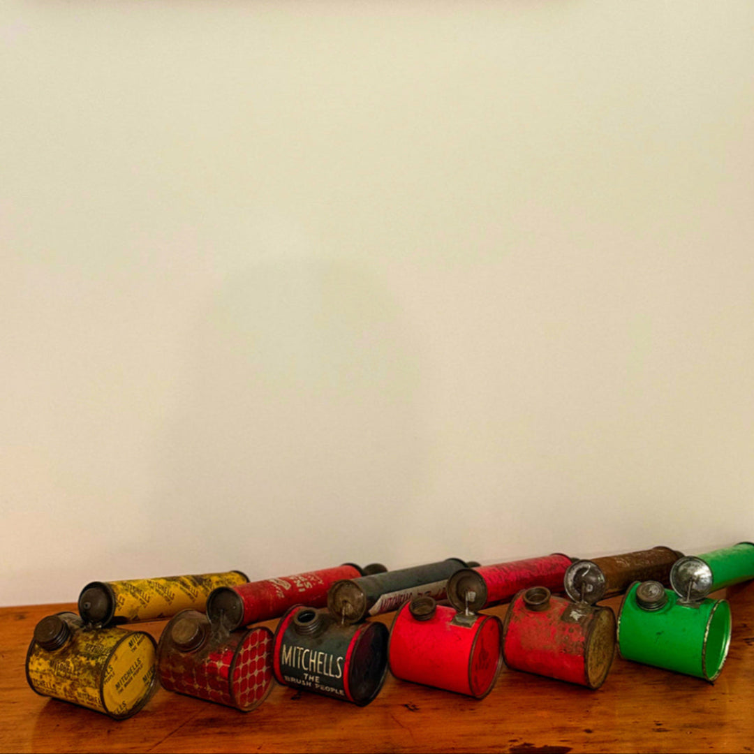 Collection of vintage metal cans with different colors on a wooden surface against a white wall.