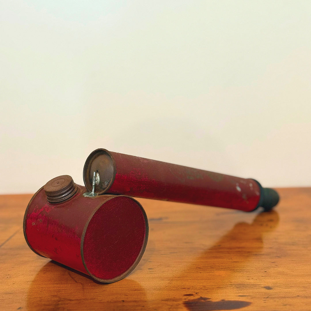 Vintage red insect spray hand pump with a worn exterior and metal cap, displayed on a wooden surface showcasing its retro design.