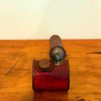 Vintage red insect spray hand pump with a worn exterior and metal cap, displayed on a wooden surface showcasing its retro design.