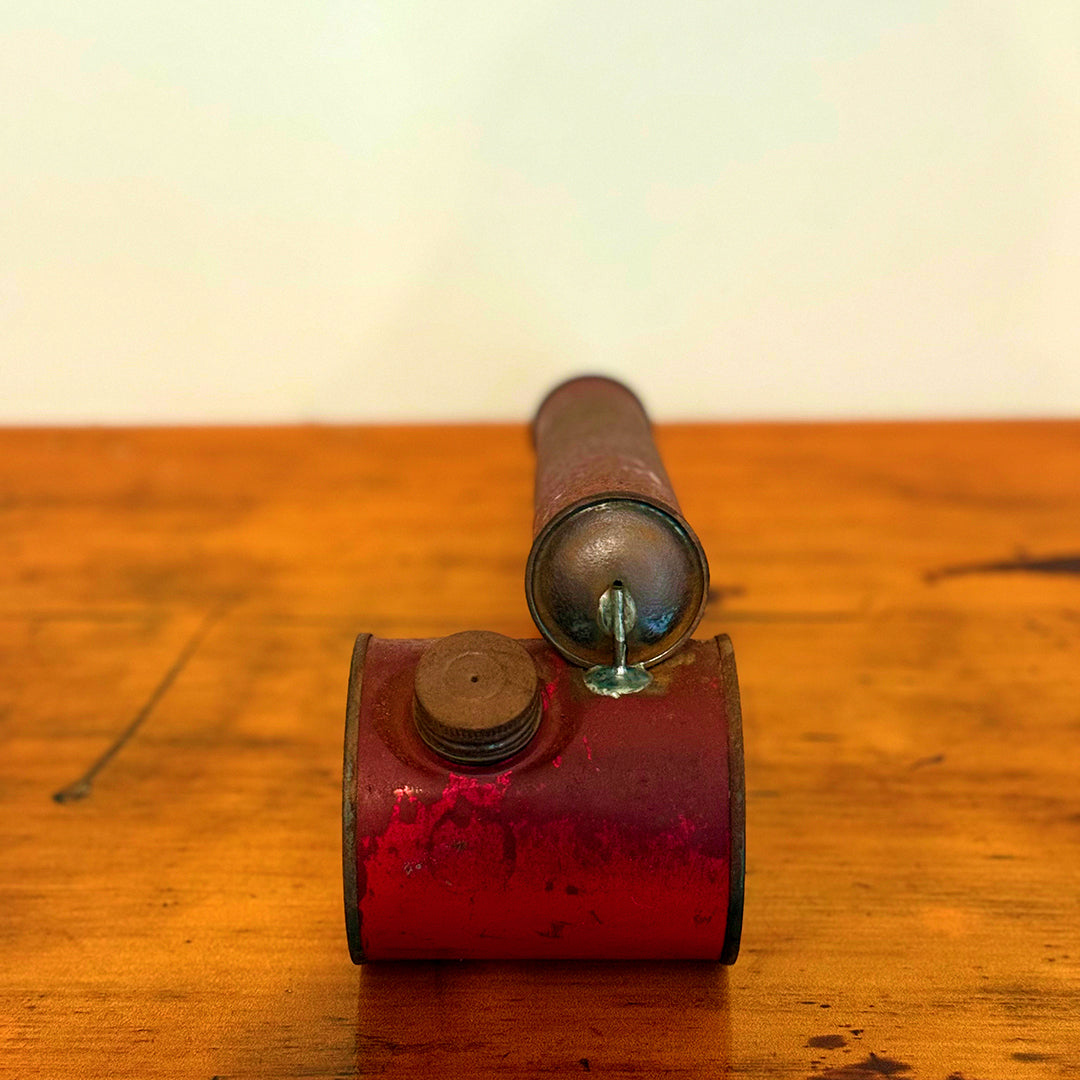 Vintage red insect spray hand pump with a worn exterior and metal cap, displayed on a wooden surface showcasing its retro design.