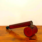Vintage red insect spray hand pump with a worn exterior and metal cap, displayed on a wooden surface showcasing its retro design.