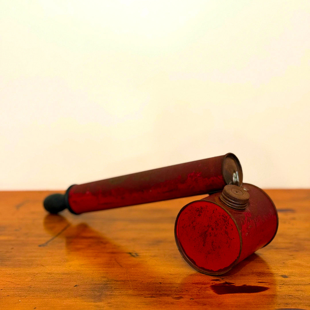 Vintage red insect spray hand pump with a worn exterior and metal cap, displayed on a wooden surface showcasing its retro design.