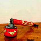 Vintage Mortein insect spray hand pump featuring a red body with the slogan "When you’re onto Mortein, Stick to it!" and classic Mortein dog logo. A retro collectible piece on a wooden surface.