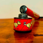 Vintage Mortein insect spray hand pump featuring a red body with the slogan "When you’re onto Mortein, Stick to it!" and classic Mortein dog logo. A retro collectible piece on a wooden surface.
