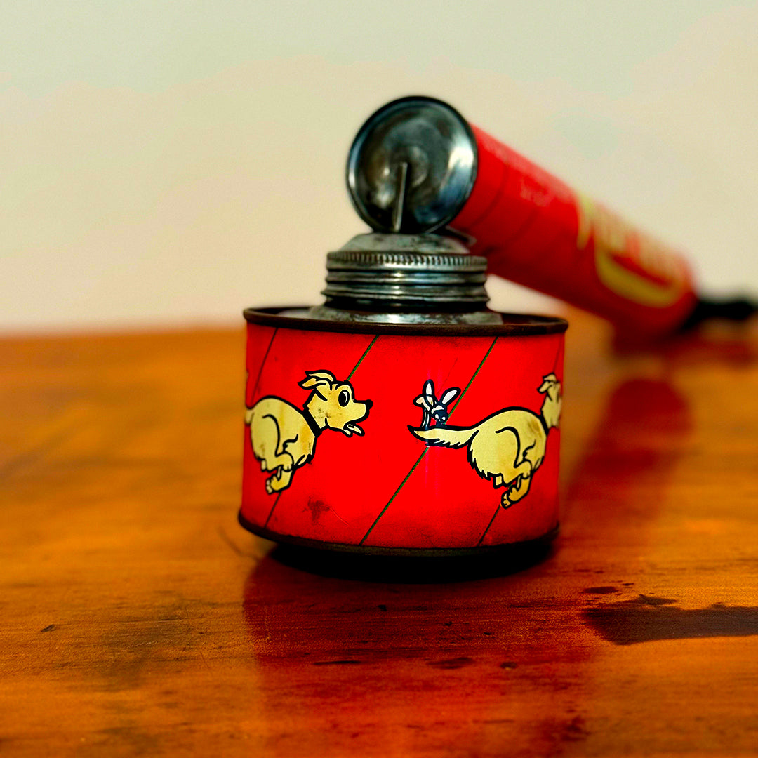 Vintage Mortein insect spray hand pump featuring a red body with the slogan "When you’re onto Mortein, Stick to it!" and classic Mortein dog logo. A retro collectible piece on a wooden surface.
