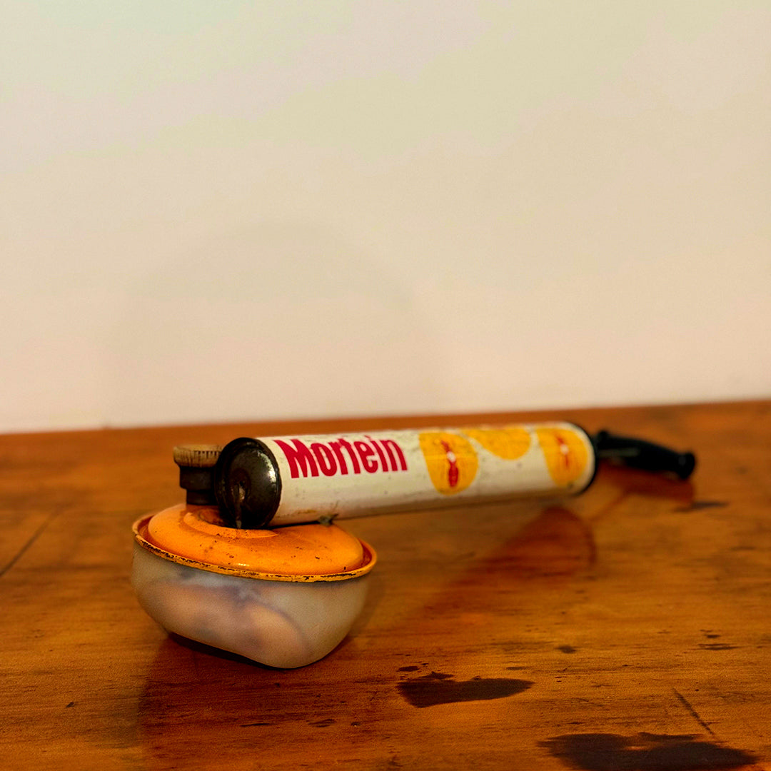 Vintage Mortein insect spray hand pump with an orange base, featuring the classic Mortein logo and vintage design, displayed on a wooden surface.