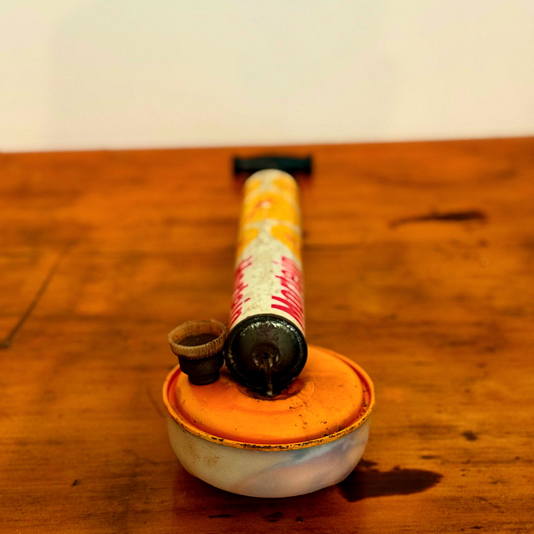 Vintage Mortein insect spray hand pump with an orange base, featuring the classic Mortein logo and vintage design, displayed on a wooden surface.