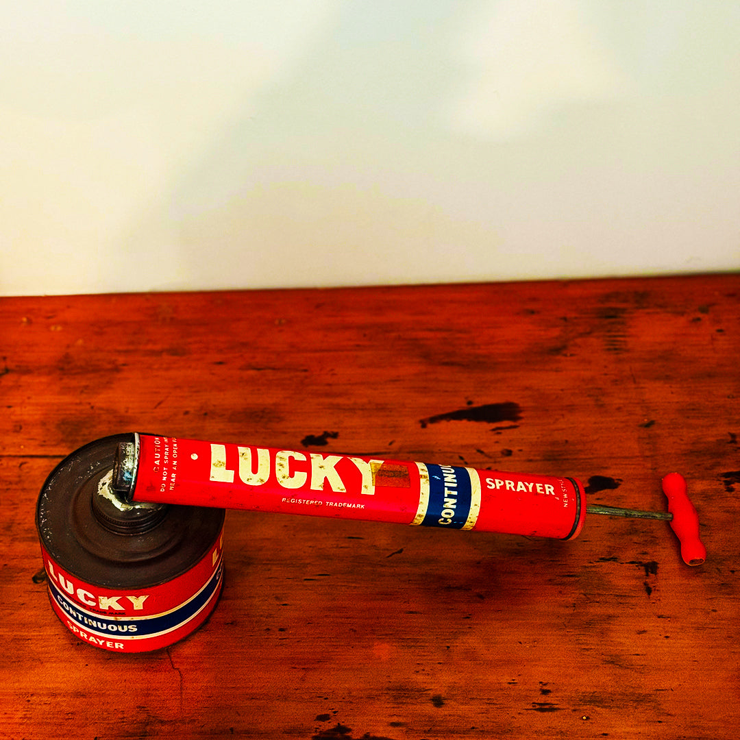 Vintage Lucky Sprayer with a red and blue design, showcasing a hand pump insecticide dispenser on a wooden surface.