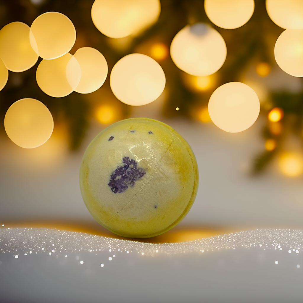 A yellow and cream bath bomb with a lavender-purple centre, photographed with soft golden Christmas lights and a festive background. A handcrafted Australian bath bomb from Luxe & Humble, perfect for gifting, pamper hampers and everyday self-care.
