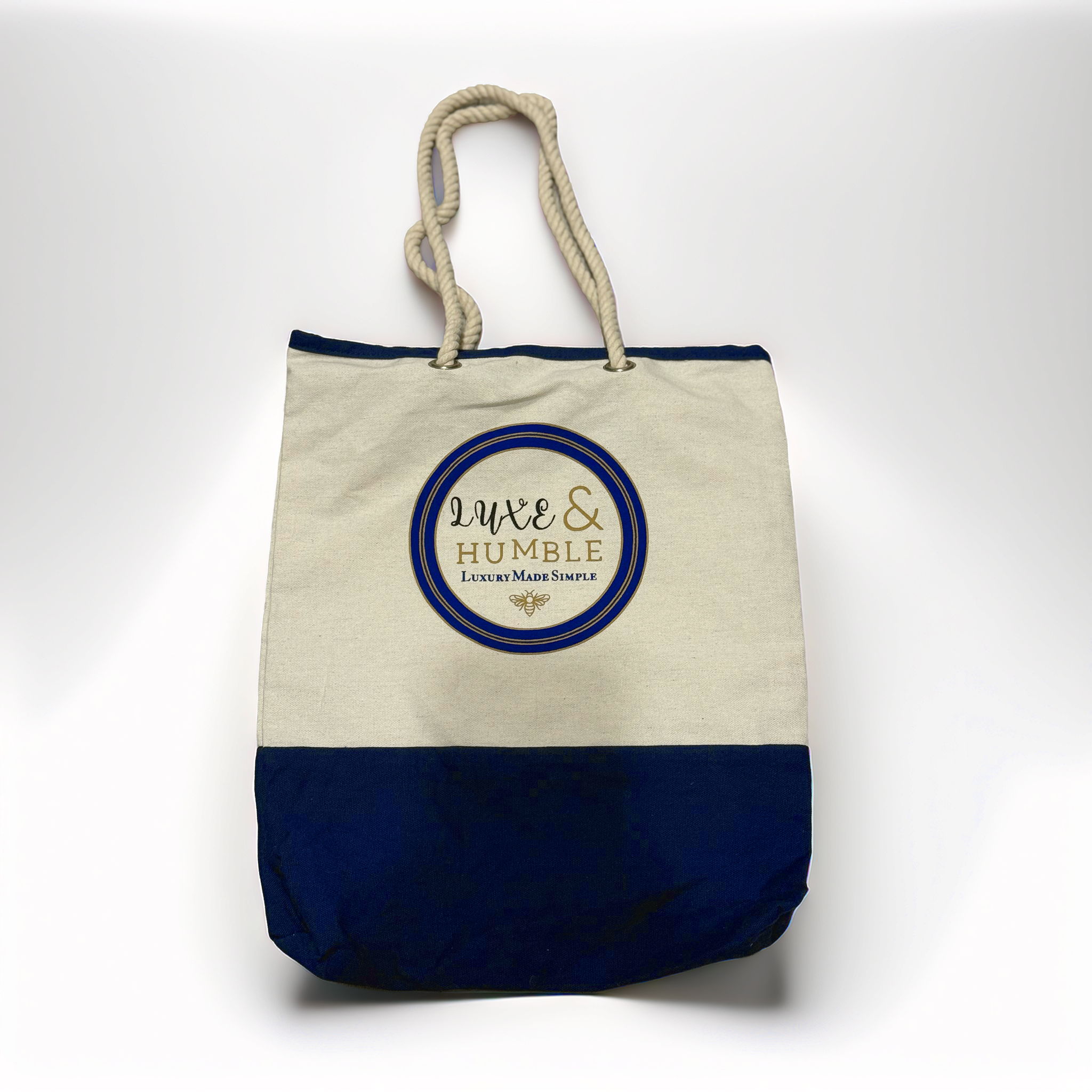 A high-quality product photo of the Luxe & Humble canvas tote bag displayed upright on a clean white background. The bag features a natural canvas upper, navy base, thick rope handles, and the signature Luxe & Humble round logo. Crisp, clear and ideal for Australian shoppers wanting a detailed view of the bag’s design and craftsmanship.