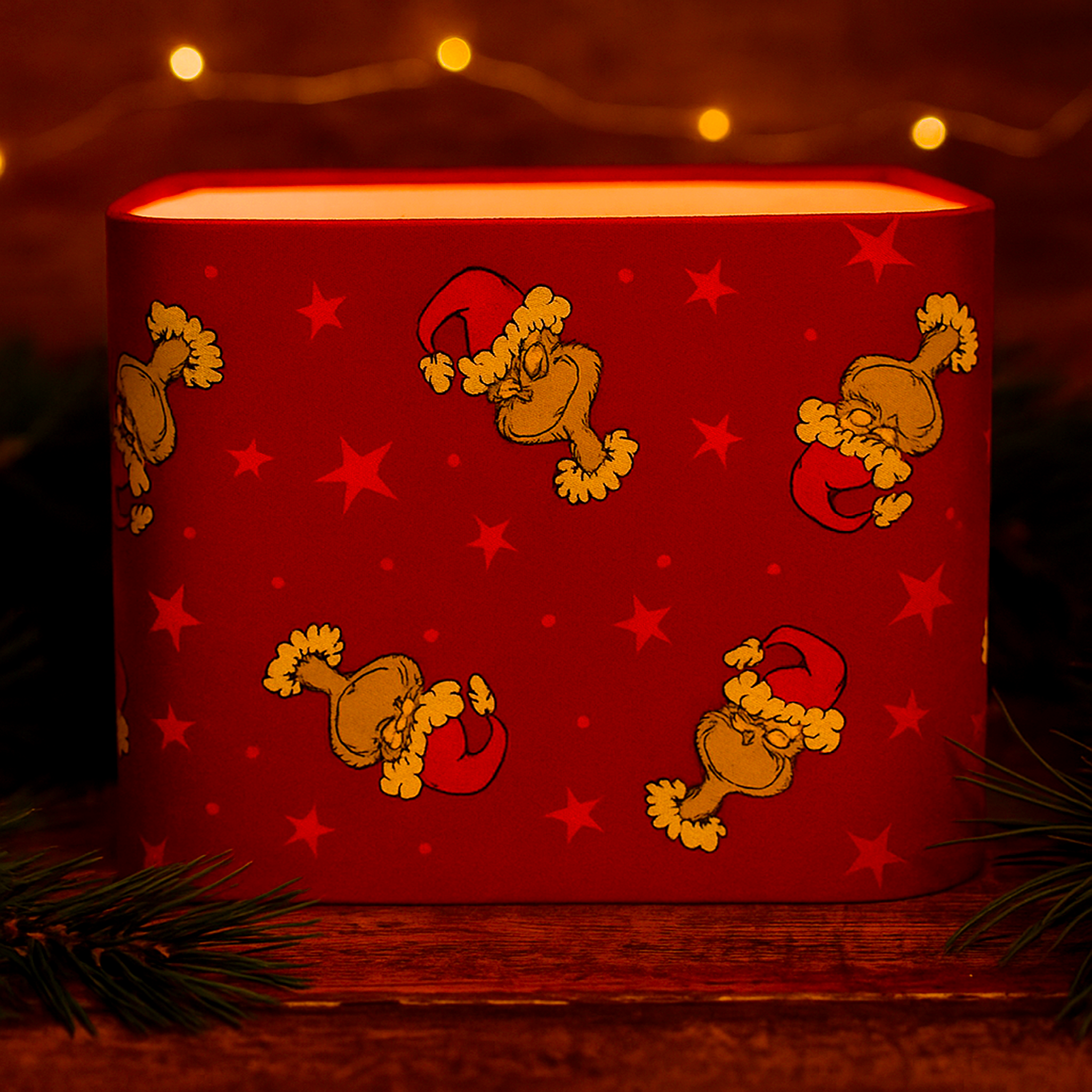 Handmade Luxe & Humble rectangular 20 x 40 cm Christmas lampshade featuring vibrant red cotton fabric with playful Grinch Santa print and star details, glowing warmly on a rustic pine shelf surrounded by pinecones and festive greenery. Crafted in Australia, perfect for holiday home décor.