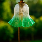 Close-up of an elegant glass lampshade in golden yellow and emerald green tones with delicate etched floral patterns, glowing warmly with light. Styled outdoors with a soft natural background, this Luxe and Humble piece highlights craftsmanship and artistry in decorative lighting.