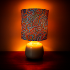 Table lamp featuring ‘Whirlwind Country’ dot artwork by Pauline Napangardi Gallagher. The vibrant fabric shade showcases intricate swirls in blue, red, and orange tones, paired with a white ceramic base. Styled with warm lighting, this Luxe and Humble décor piece blends authentic Indigenous art with contemporary home design.