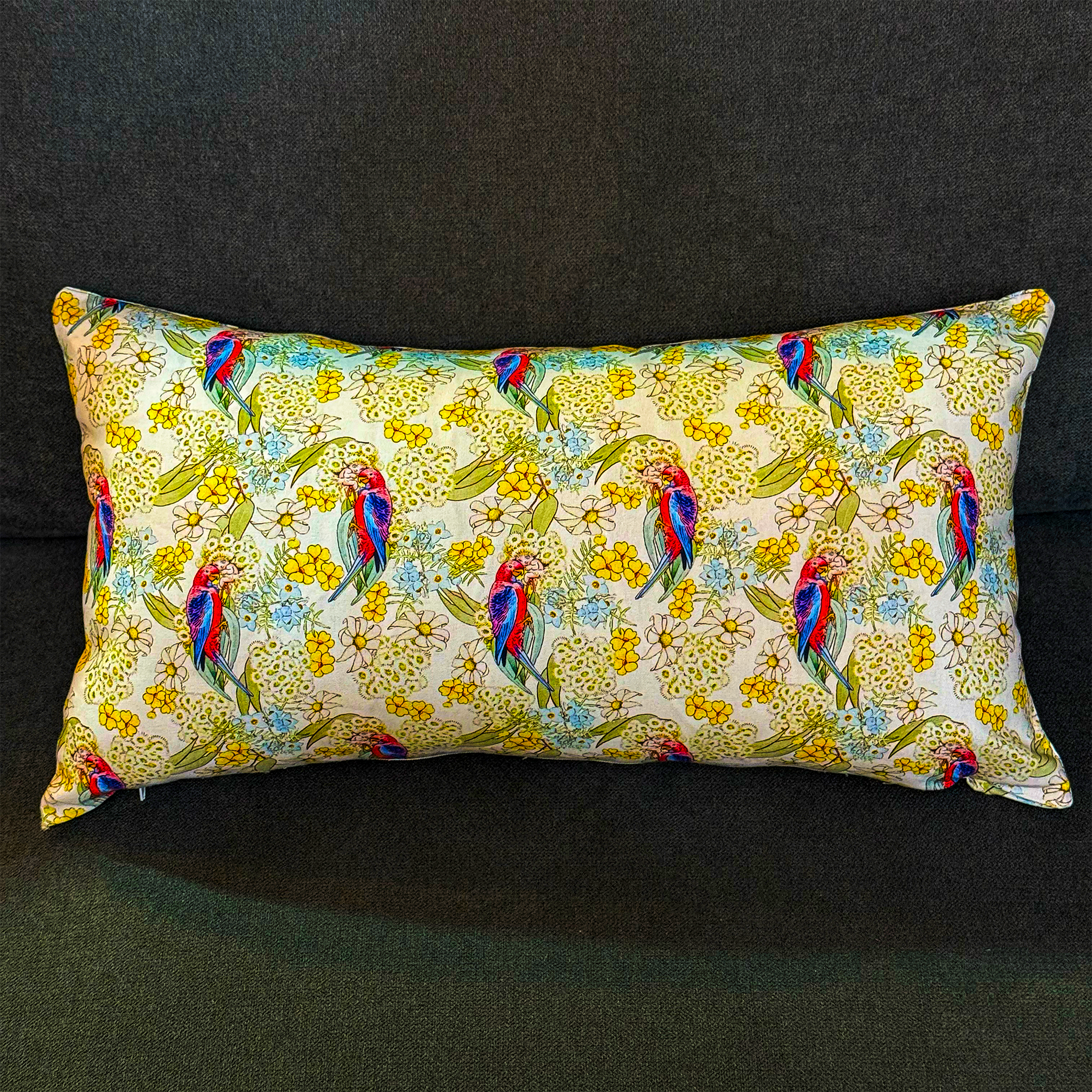 Rectangular decorative cushion by Luxe and Humble featuring an Australian native parrot in striking pink, blue, and red plumage, surrounded by yellow and pastel botanical flowers on a soft cream background. This designer cushion brings a vibrant, tropical Australian touch to interiors, ideal for styling sofas, beds, or accent chairs.