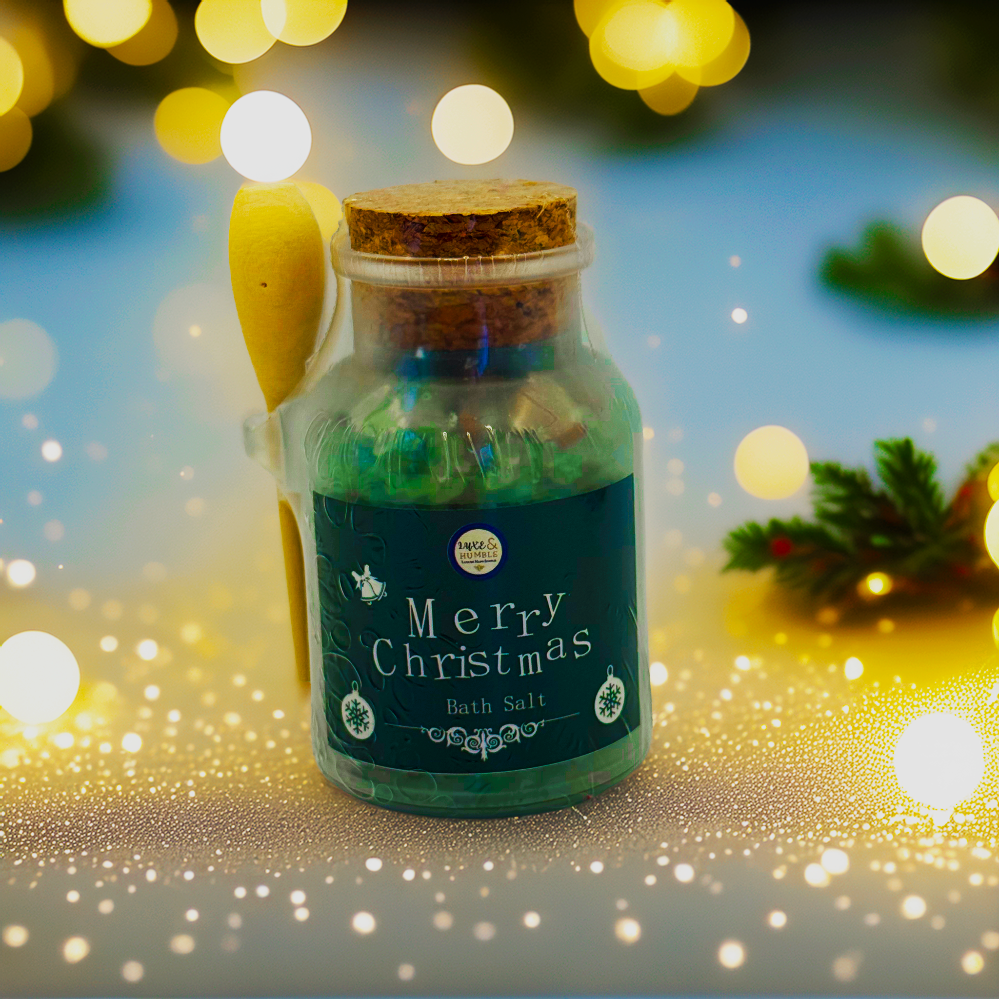 Green-label Merry Christmas Bath Salt in a vintage glass jar with cork lid and wooden spoon, displayed in front of warm golden Christmas bokeh lights and soft festive sparkles. Handmade holiday bath salt by Luxe & Humble, Australia.