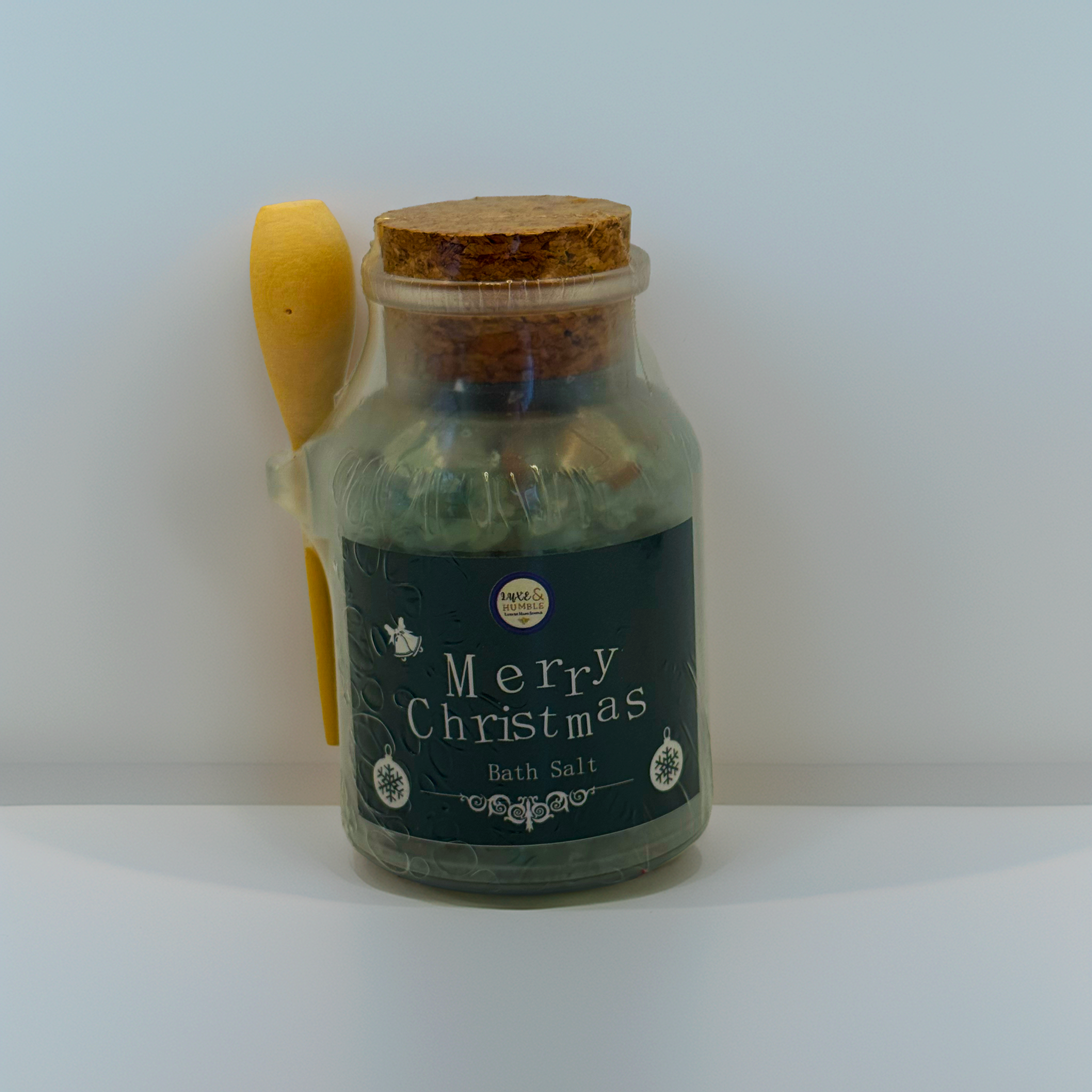 Green-label Merry Christmas Bath Salt in a clear apothecary jar with cork lid and wooden spoon, photographed on a clean studio white background. Handmade festive bath salt by Luxe & Humble.