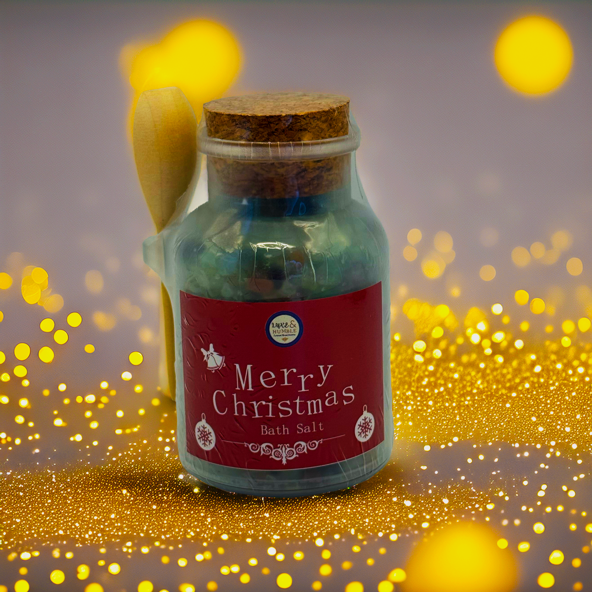 Red-label Merry Christmas Bath Salt in a glass jar with wooden scoop and cork lid, photographed with glowing golden Christmas lights and sparkling festive accents. Luxe & Humble handmade Christmas bath salt, Australia.