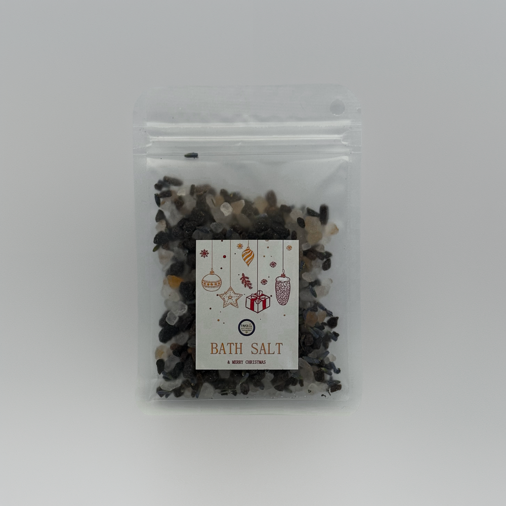 A Luxe & Humble Midnight Charcoal Christmas Bath Salt in a clear resealable pouch filled with dark charcoal mineral salts and light crystal accents. The festive label features hanging Christmas ornaments, stars and a gift illustration. Set against a clean studio background, this handcrafted Australian bath salt is ideal for Christmas gifting, stocking fillers and luxury self-care.