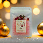 A Luxe & Humble Rose Blush Christmas Bath Salt displayed in a clear resealable pouch filled with pink mineral salts and dried rose petals. The festive front label features hanging Christmas ornaments, stars and a gift illustration. Styled with glowing golden baubles, warm bokeh lights and soft sparkles, this product image captures a luxurious and cosy holiday feel, perfect for Australian Christmas gifting, stocking fillers and self-care lovers.