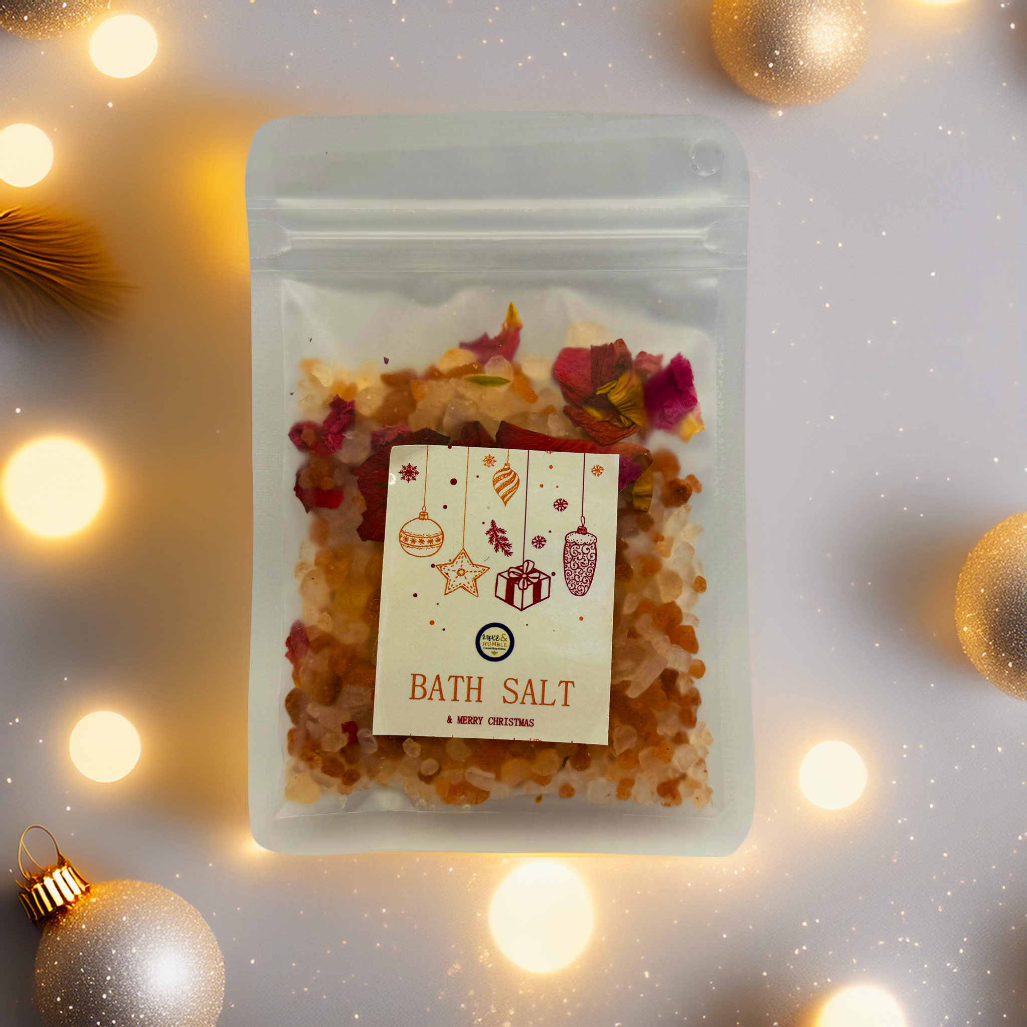 A Luxe & Humble Sunset Rose Christmas Bath Salt in a clear pouch filled with warm orange mineral salts and dried rose petals. The festive Christmas label features ornaments, stars and a gift illustration. Photographed on a clean studio background, this handcrafted Australian bath salt is ideal for Christmas gifting, stocking fillers and luxury self-care.