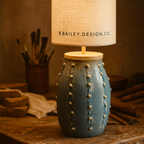 The Coastal Clay Lamp Base by B.Bailey.Design.Co., handcrafted in Australia from textured ceramic with ocean-blue glaze and timber top. Styled in a warm artisan studio with soft lighting and linen tones, showcasing authentic Australian craftsmanship and timeless coastal design.