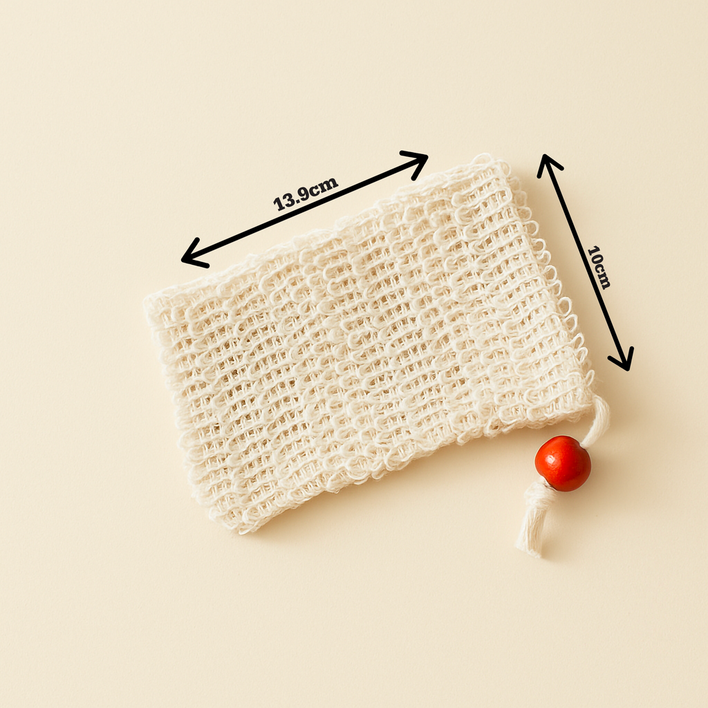 Close-up of The Purity Pouch exfoliating soap saver bag made from natural sisal, featuring a red wooden bead drawstring, photographed against a soft cream backdrop — minimalist and organic in tone.