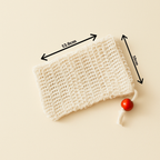Close-up of The Purity Pouch exfoliating soap saver bag made from natural sisal, featuring a red wooden bead drawstring, photographed against a soft cream backdrop — minimalist and organic in tone.