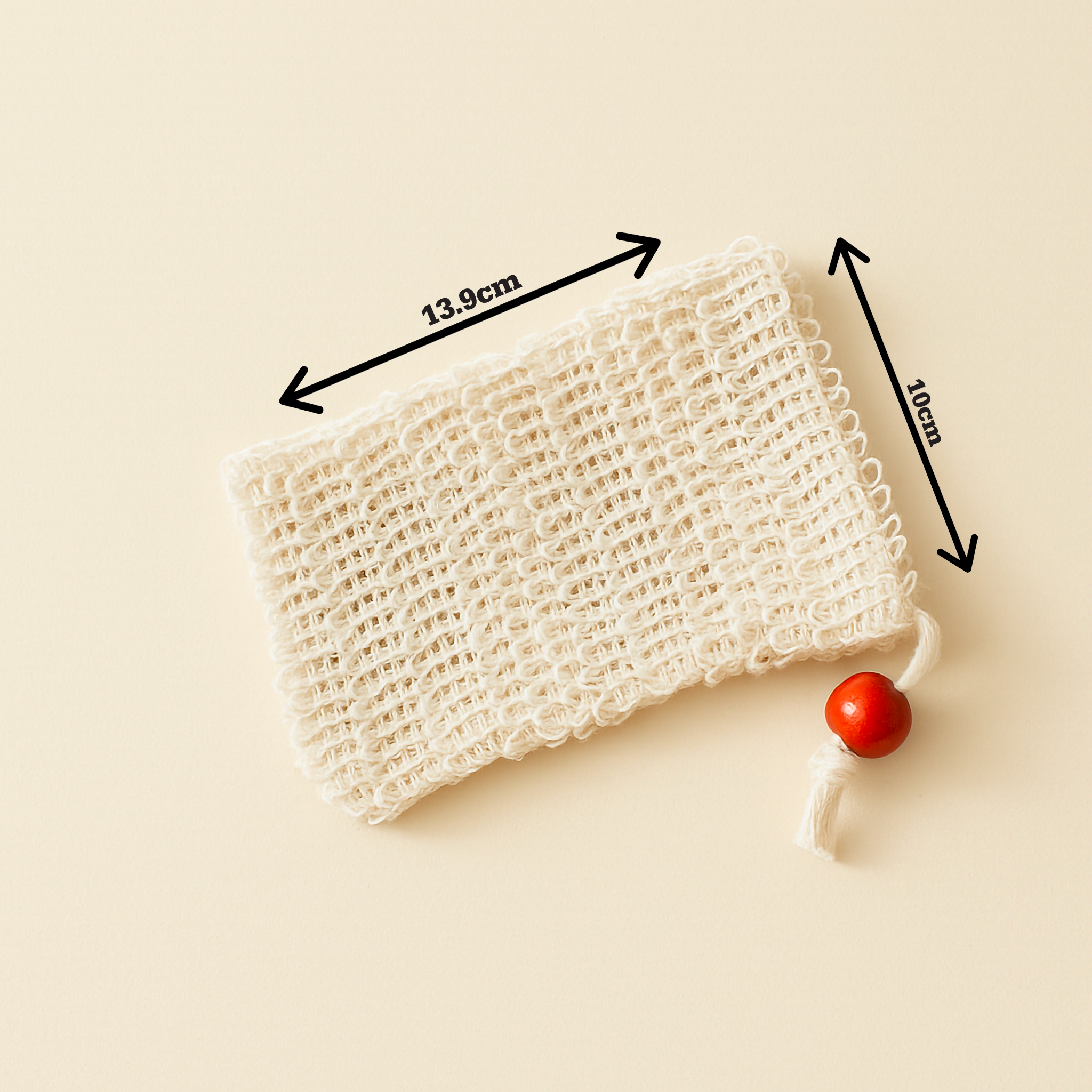 Close-up of The Purity Pouch exfoliating soap saver bag made from natural sisal, featuring a red wooden bead drawstring, photographed against a soft cream backdrop — minimalist and organic in tone.